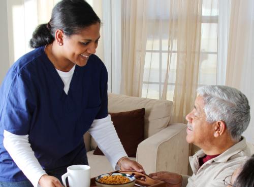 Photo of a care worker giving a meal to an elderly man 