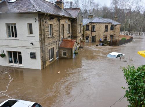 Flood water surrounding buildings and covering two cars. 