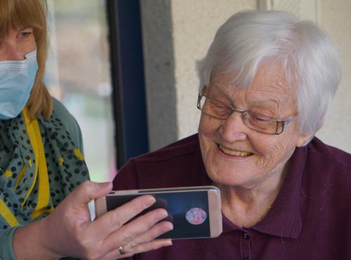 Older lady shown a photo on a phone by care staff.