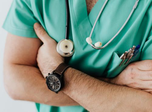 Doctor crossing their arms. Wearing medical gear and a watch.