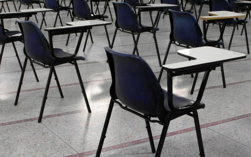 A school chair and desk sits in a cold and clinical looking exam hall